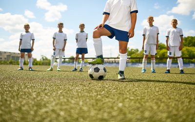 Low section portrait of football captain standing in center of field stepping on ball with the rest of team in background