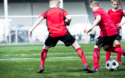 Full length back view portrait of teenage boys playing football during practice of junior team in stadium, copy space