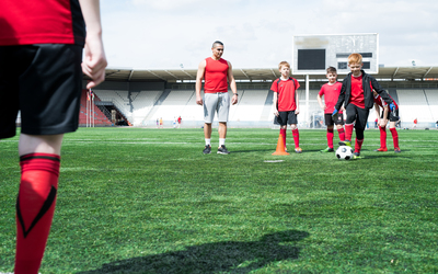 Full length portrait of junior football team practice, focus on red haired teenage boy leading ball, copy space